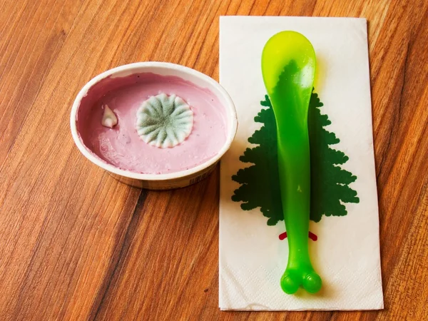 Plastikbecher mit rosa Fruchtjoghurt mit hässlicher Kreisblüte aus giftigem Schimmel. gelb-grüner Plastiklöffel. — Stockfoto