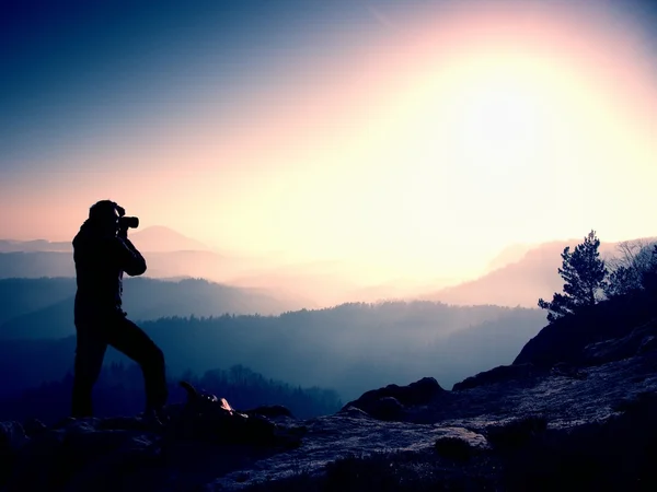 专业摄影师的照片带镜相机的岩峰上。梦幻般顽固景观、 春橙色粉红色雾日出. — 图库照片