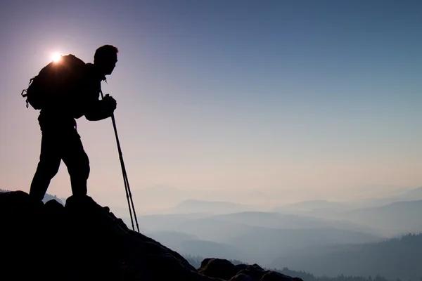 Reiseführer zeigen den richtigen Weg mit der Stange in der Hand. Wanderer mit sportlichem Rucksack stehen auf felsigem Aussichtspunkt über nebligem Tal. Sonnenaufgang im Frühling in den felsigen Bergen. — Stockfoto