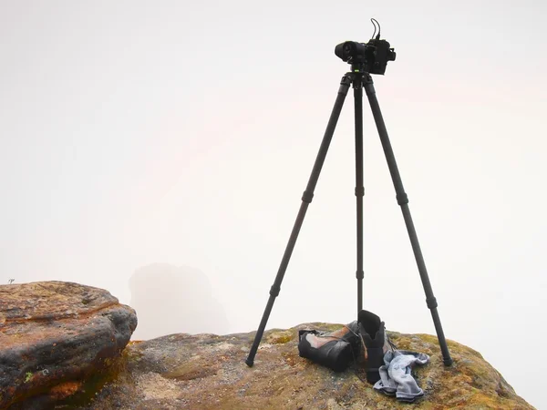 Waiting for a moment. Big professional camera on a basalt tripod on mountain peak. Bellow fogy landscape background. — Stock Photo, Image