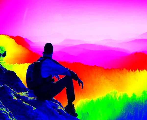 Fantastisk infraröd skanning. Turist med stolpar och stora ryggsäck stående på klippiga utsiktsplats och titta in i dimmiga morgon landskap. Melankolisk höst morgon. Termografi färger. — Stockfoto