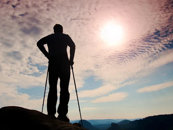 Силуэт туриста с большим рюкзаком и палками в руках. Солнечный красочный рассвет в скалистых горах. Человек стоит на скалистой точке над туманной долиной . — стоковое фото