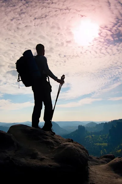 Silueta de excursionista con gran mochila y bastones en las manos. Soleado amanecer colorido en las montañas rocosas. Hombre de pie en el punto de vista rocoso sobre el valle brumoso . —  Fotos de Stock