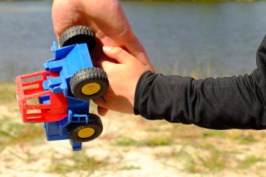 Babanın büyük el plastik oyuncak kamyon küçük bir çocuk elini ver. Mavi ve siyah gömlek elinde.