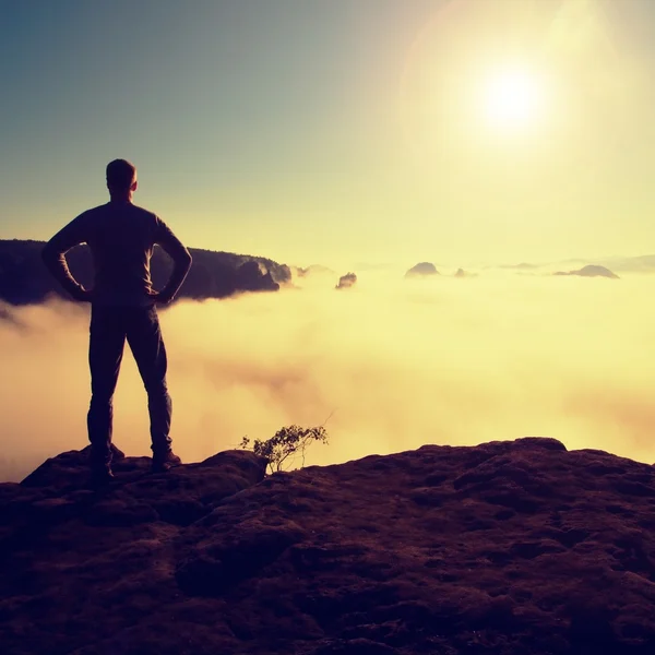 El hombre de camisa y jeans está de pie en la cima del imperio de piedra arenisca y vigilando el brumoso y brumoso valle matutino hasta el Sol. — Foto de Stock