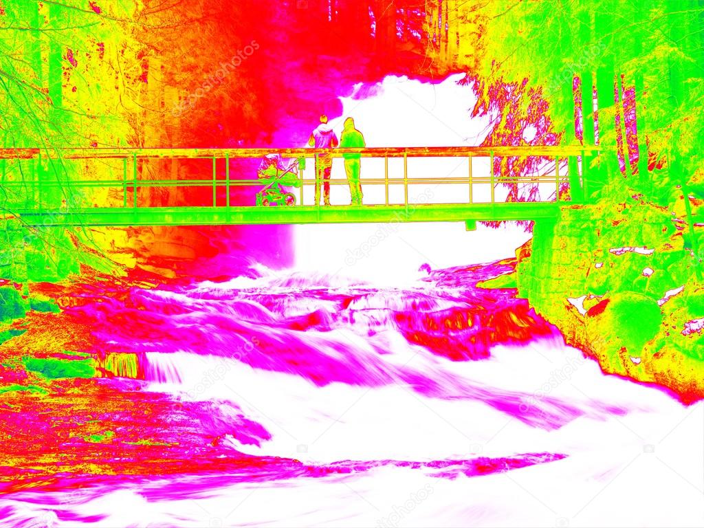 Foamy water of waterfall, bellow footpath bridge with people. Cold water of mountain river in infrared photo. Amazing thermography. 