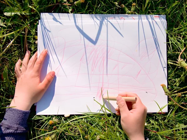 Vista da vicino della mano del bambino che disegna ornamenti colorati su carta. Quaderno in erba fresca verde di prato . — Foto Stock