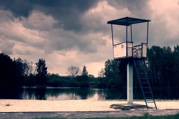 En gammal vit och Rostig metall badvakt tornet med stol på en damm strand — Stockfoto