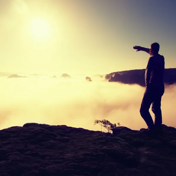 Man in shirt and jeans is standing on the peak of sandstone empire  and watching over the misty and foggy morning valley to Sun. Beautiful moment the miracle of nature — Stock Photo, Image