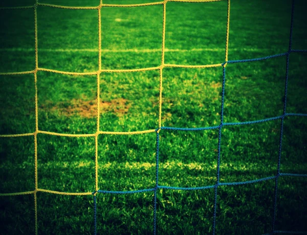 Detail der gelb blau gekreuzten Fußballnetze, Fußball im Tornetz mit grünem Gras auf dem Spielplatz im Hintergrund. — Stockfoto