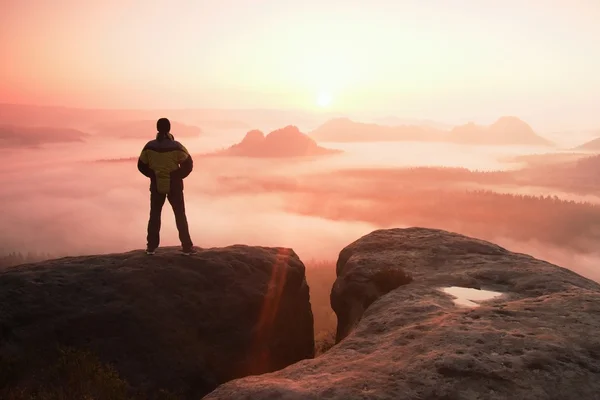 Moment of loneliness. Man on the rock empires  and watch over the misty and foggy morning valley to Sun