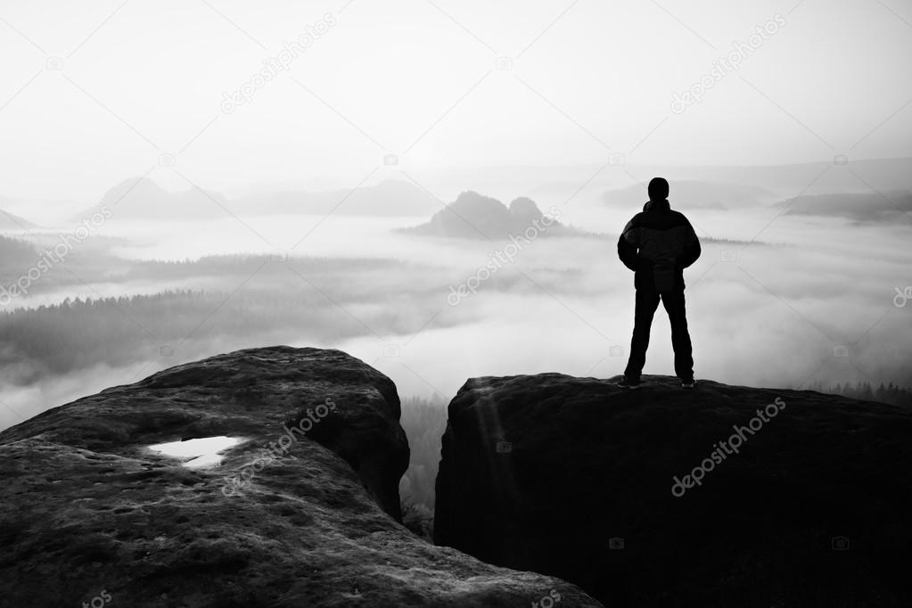 Moment of loneliness. Man on the rock empires  and watch over the misty and foggy morning valley to Sun