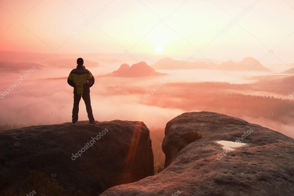 Moment of loneliness. Man on the rock empires  and watch over the misty and foggy morning valley to Sun