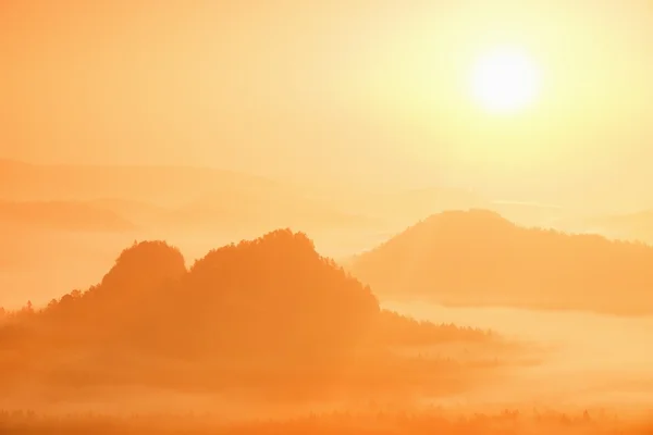 Misty landscape with fog between hills and orange sky within sunrise — Stock Photo, Image