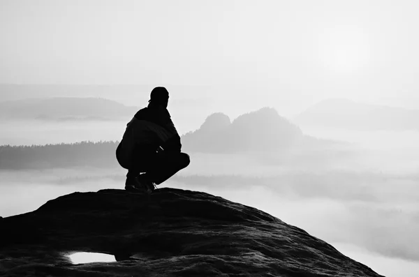 Vista trasera del caminante masculino sentado en el pico rocoso mientras disfruta de un colorido amanecer sobre el valle de las montañas —  Fotos de Stock