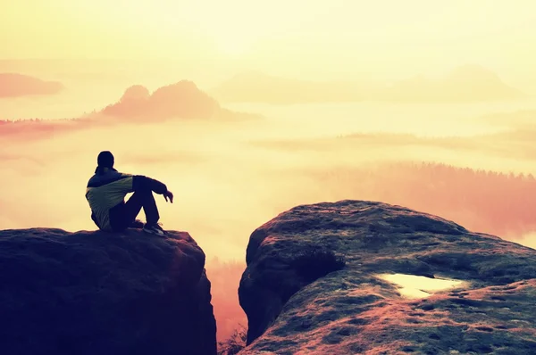 Achteraanzicht van mannelijke wandelaar zittend op de rotsachtige piek terwijl u geniet van een kleurrijke daybreak boven mounrains vallei — Stockfoto