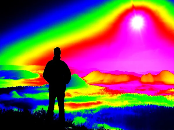Escaneamento infravermelho fantástico. turista cansado no pico rochoso. Maravilhoso amanhecer nas montanhas, névoa de laranja pesada em valle profundo — Fotografia de Stock