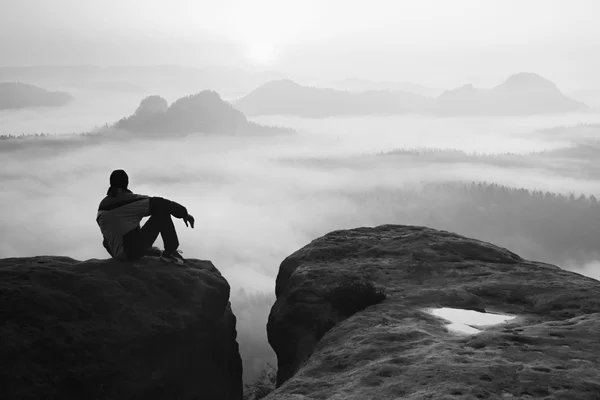 Rückansicht eines männlichen Wanderers, der auf dem felsigen Gipfel sitzt und einen farbenfrohen Tagesanbruch über dem Bergtal genießt — Stockfoto