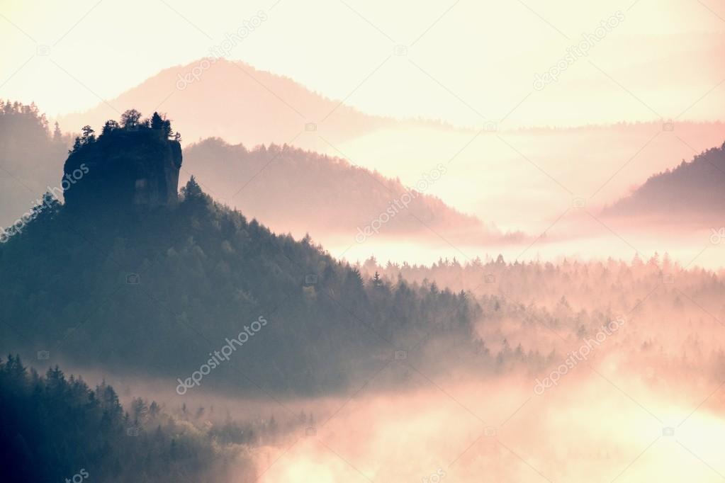 Misty landscape with fog between hills and orange sky within sunrise