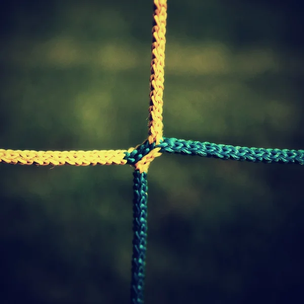 Detail of yellow blue crossed soccer nets, soccer football in goal net with green grass on playground in the background. — Stock Photo, Image