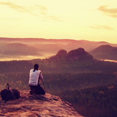 Beyaz ceketli profesyonel fotoğrafçı kayalık tepe üzerinde tripod üzerinde kamera ile fotoğraf çeker. Rüya gibi adamlara manzara, Bahar Turuncu pembe puslu sunrise bir güzel vadi