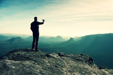 Uzun boylu uzun yürüyüşe çıkan kimse fotoğraf dağ tepe üzerinde akıllı telefonla güneş doğarken alıyor.