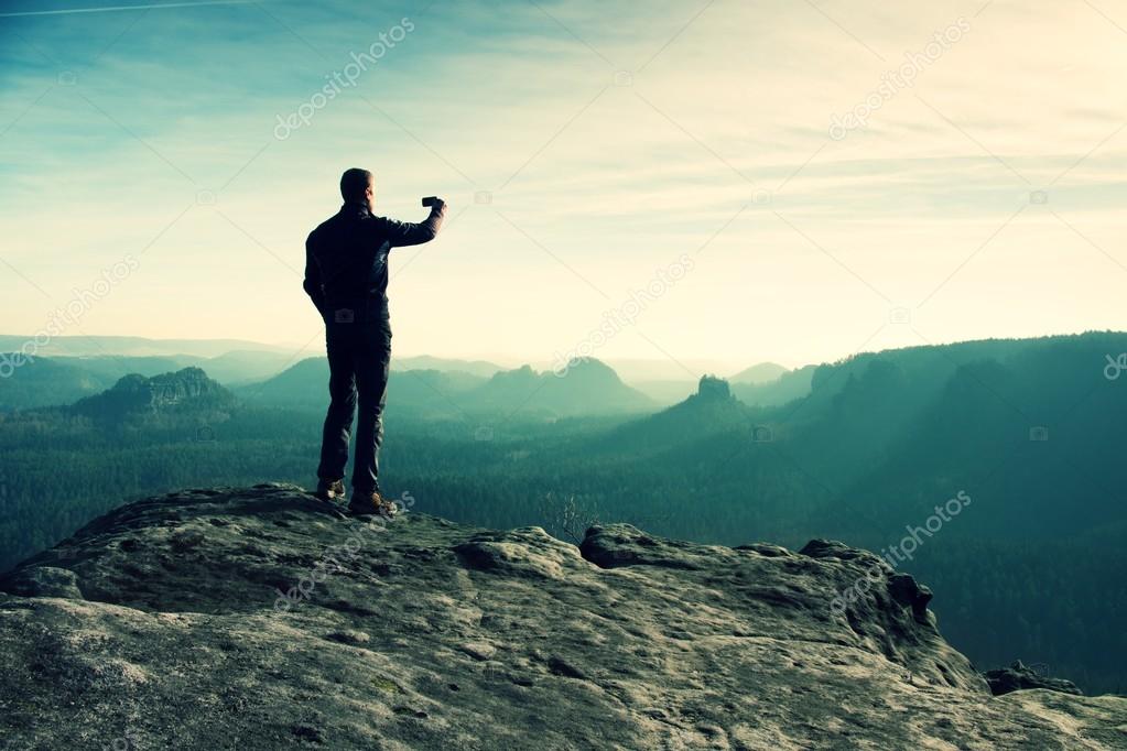 Tall hiker is taking photo by smart phone on the peak of mountain at sunrise.  Stock Photo by ©rdonar 76668857