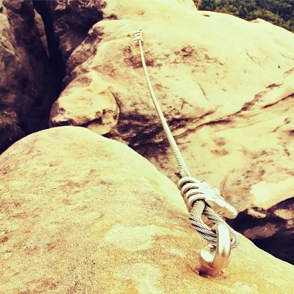 Detail of steel bolt anchor eye and rope end anchored into sandstone rock. Iron twisted rope fixed in block by screws snap hooks. — Stock Photo, Image
