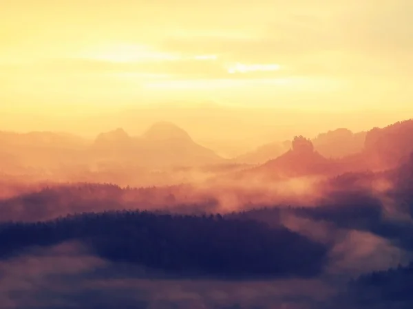 Sunrise in a beautiful mountain of Czech-Saxony Switzerland. Hilly peaks increased from orange fog with sun rays.