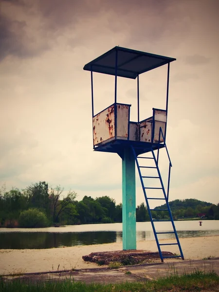 Старая белая и ржавая металлическая спасательная башня со стулом на берегу озера . — стоковое фото