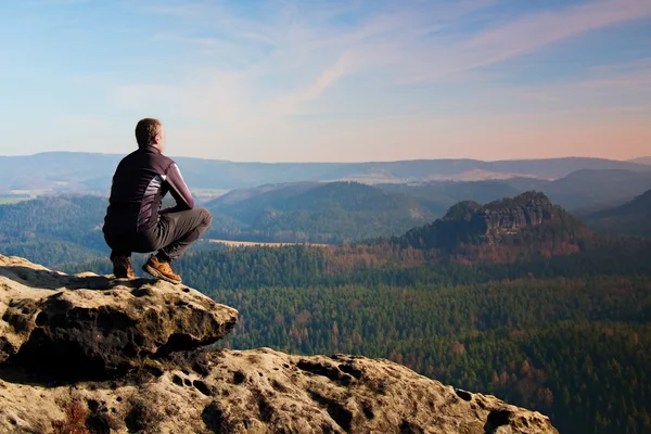 Climbing adult man at the top of  rock with beautiful  aerial view of the deep misty valley bellow — Stock Photo, Image