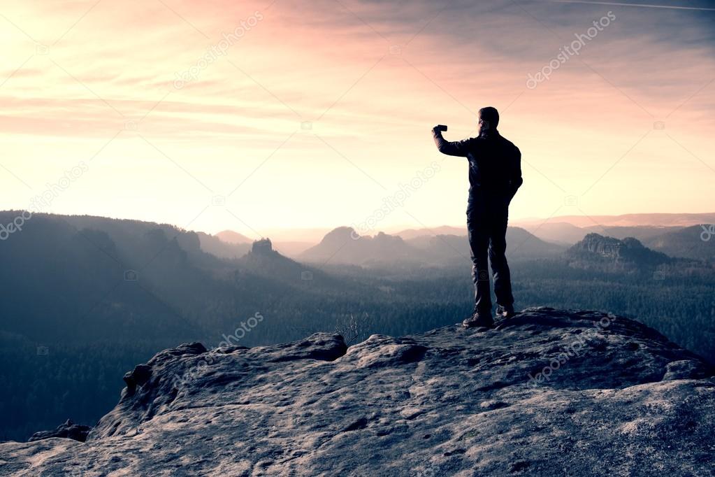 Young Man In Black Sportswear Is Sitting On Cliff Edge And Looking To Misty Valley Bellow Young Man In Black Sportswear Is Sitting On Cliff Edge And Looking To Misty Valley Bellow