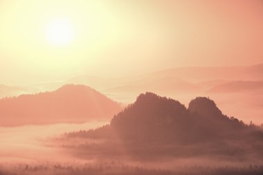 Misty landscape with fog between hills and orange sky within sunrise
