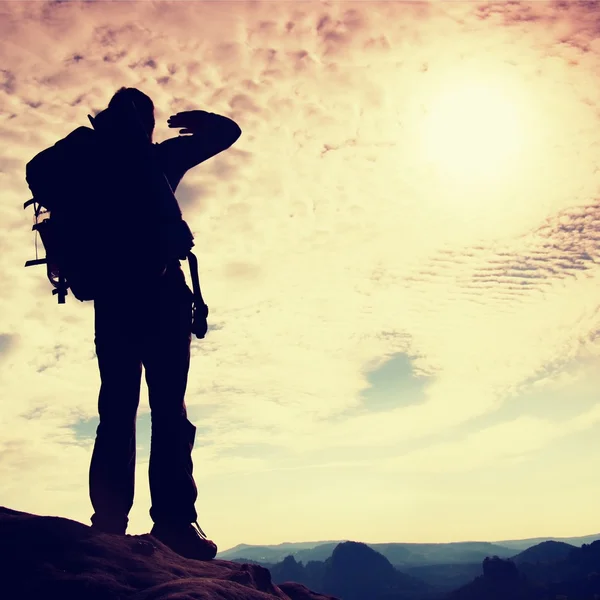 Turista con gran mochila de pie en el punto de vista rocoso y mirando en profundo valle brumoso a continuación. Amanecer soleado de primavera en montañas rocosas . — Foto de Stock
