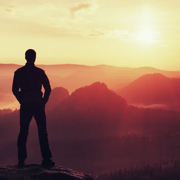 Escursionista in nero in piedi sulla cima nel parco imperi rocciosi e guardando sopra la nebbiosa e nebbiosa valle del mattino al sole. Bellissimo momento il miracolo della natura — Foto Stock