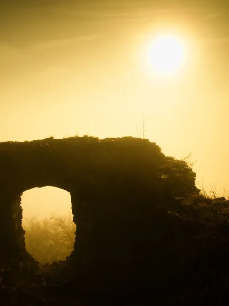 The stronghold. Stony ruin of medieval stronghold tower on hill. Early morning sunshine hidden in heavy autumn mist. — Zdjęcie stockowe