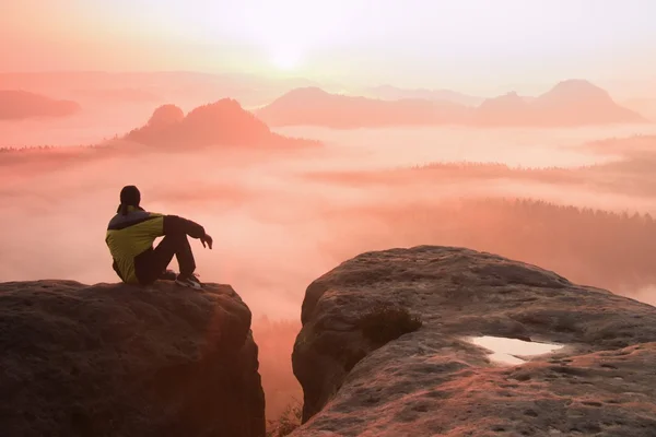 Vue arrière du randonneur assis sur le pic rocheux tout en profitant d'un lever du jour coloré au-dessus de la vallée des montagnes — Photo