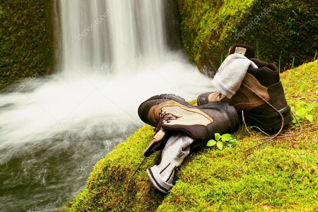 Hiker high boots and sweaty grey socks. Resting on the mossy boulder at the  nice mountain stream