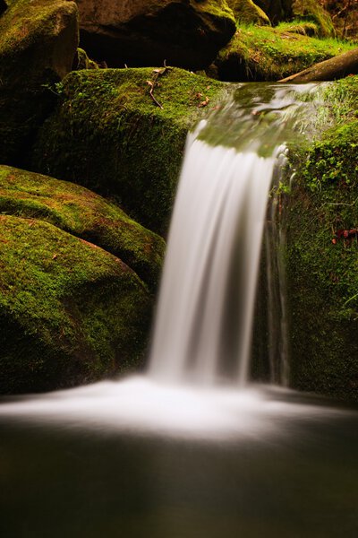Cascade on small mountain stream. Cold crystal  water is falling over basalt mossy boulders into small pool.