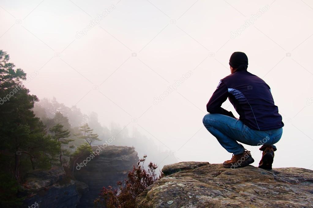 Hiker in squatting position on a rocky peak and enjoy the misty  scenery