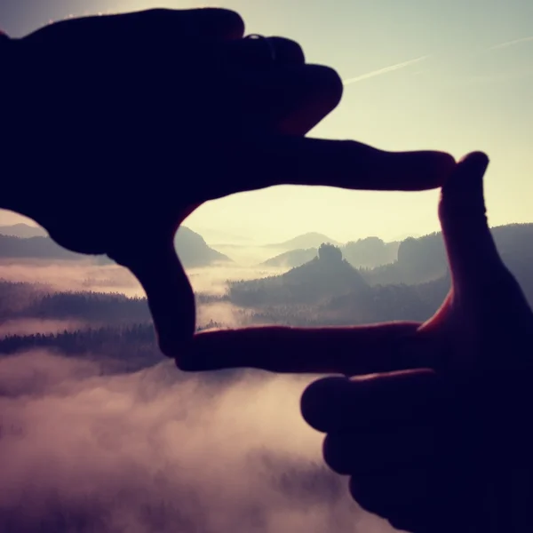 Prsty snímek. Detailní záběr rukou rám gesto. Modré mlhavé údolí pod skalnatý vrchol. Slunečné jarní v rocky mountains. — Stock fotografie