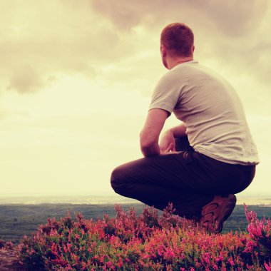 Hiker in squatting position on a rock in heather bushes, enjoy the cloudy scenery