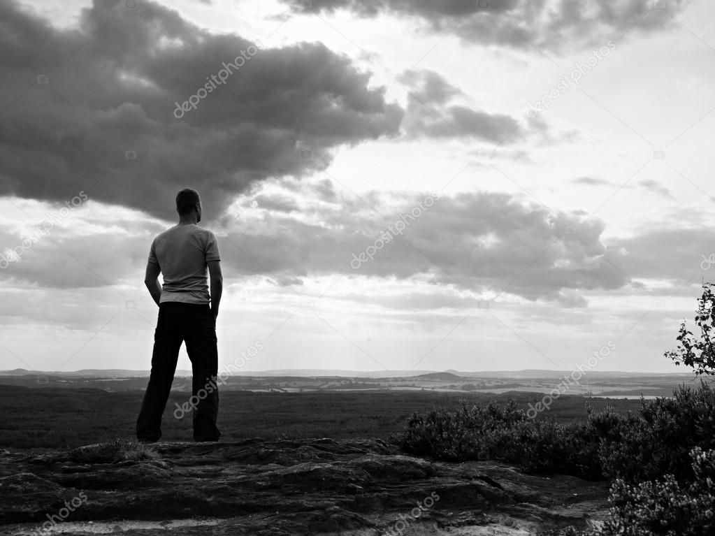 Adult sportsman in grey shirt on the cliff in rocky mountains park and watch into landscape