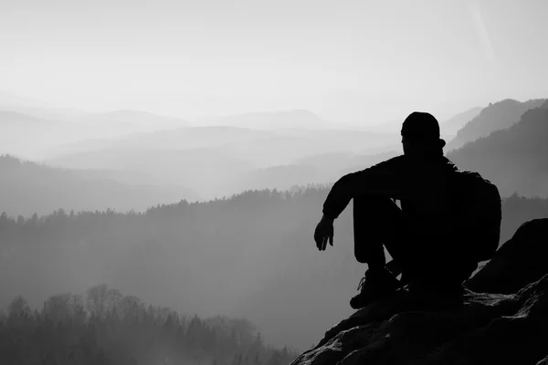 Müde Wanderer mit sportlichem Rucksack sitzen auf felsigen Gipfeln und blicken ins tief vernebelte Tal. Sonnenaufgang im Frühling in den felsigen Bergen. — Stockfoto