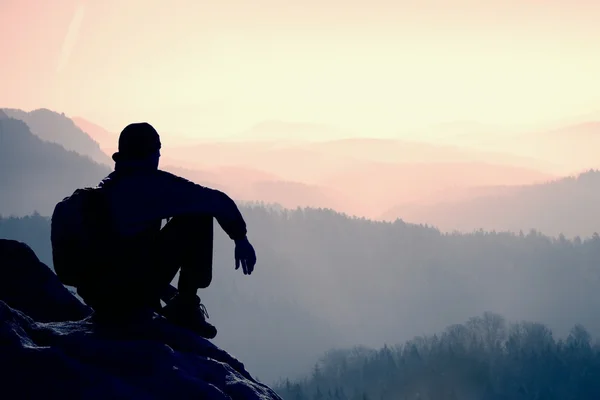 Müde Wanderer mit sportlichem Rucksack sitzen auf felsigen Gipfeln und blicken ins tief vernebelte Tal. Sonnenaufgang im Frühling in den felsigen Bergen. — Stockfoto