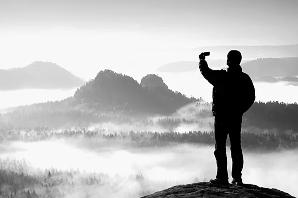 Turista alto se está tomando selfie en el pico por encima del valle. Fotografía de teléfono inteligente —  Fotos de Stock