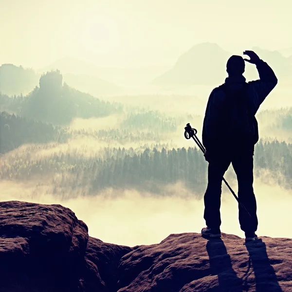 Туманный день в скалистых горах. Силуэт туриста с шестом в руке. Пеший турист стоит на скалистой точке над туманной долиной . — стоковое фото
