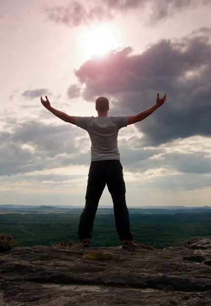 Gesto de triunfo. Feliz excursionista en camisa gris y pantalones oscuros. Hombre alto en la cima del acantilado de arenisca mirando hacia el paisaje . — Foto de Stock