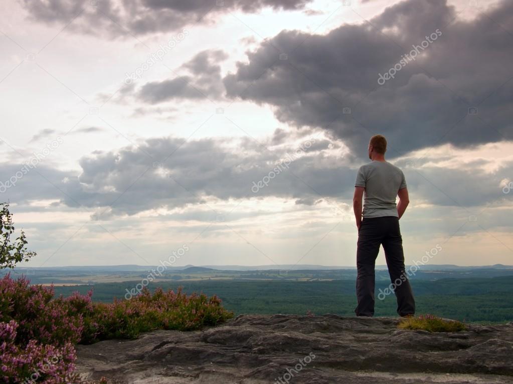 Adult sportsman in grey shirt on the cliff in rocky mountains park and watch into landscape