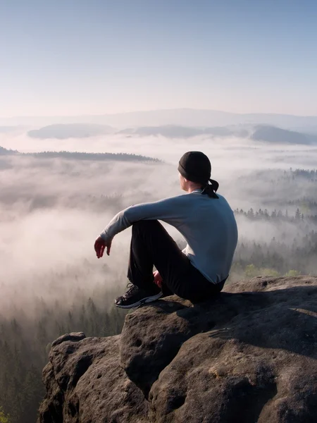 Man sitter på toppen av rock och tittar in i färgstarka dimma och dimma i skogen dalen. — Stockfoto